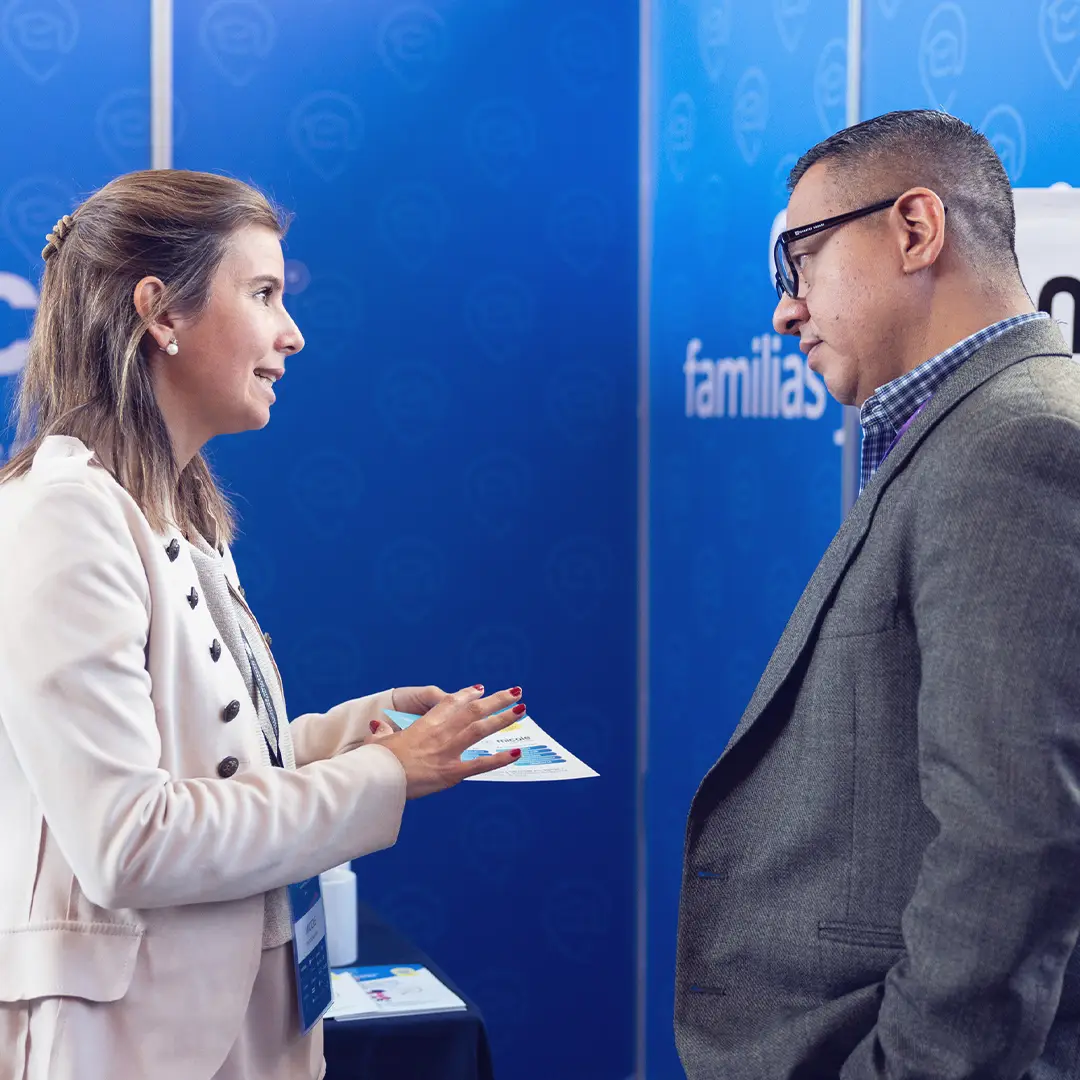Ejecutiva dialogando con empresario frente a stand de plataforma educativa